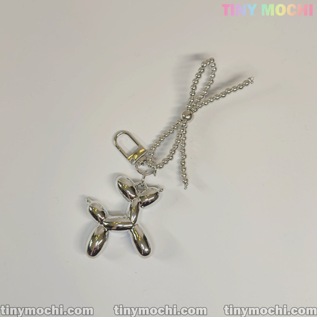 The Silver Balloon Dog Keychain with Bead Bow by Tiny Mochi features a shiny silver finish on a ball chain, with TINY MOCHI in colorful letters on a white background for a modern, trendy look—perfect as a cute bag charm or purse accessory.