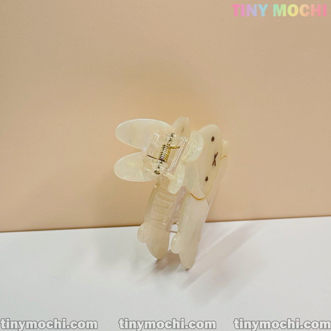 The Iridescent Bunny Hair Clip | Cute Hair Claw for Thick Hair by Tiny Mochi stands upright on a white surface, its translucent bunny face design glows subtly. Behind it, pastel TINY MOCHI text and tinymochi.com repeat on the beige background.