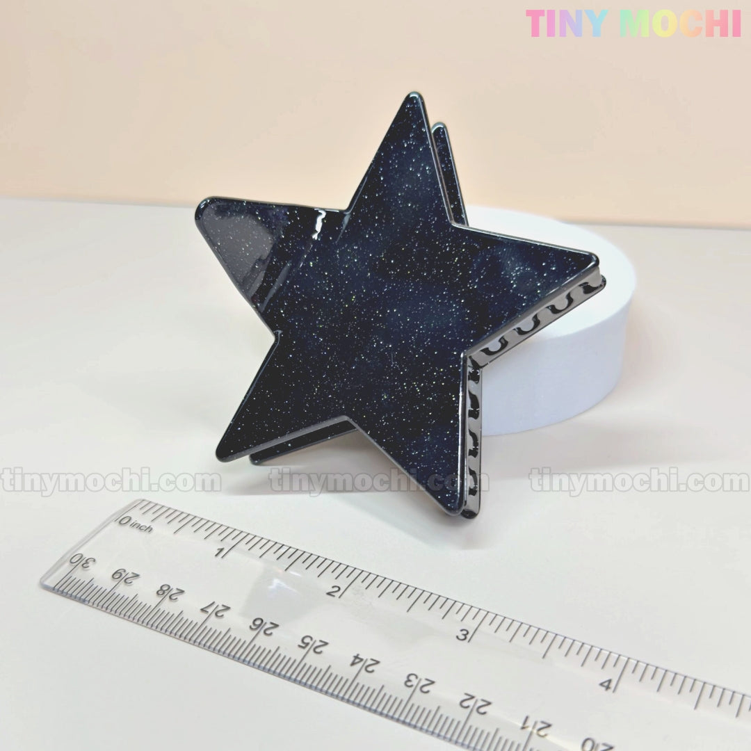 The Tiny Mochi Star Hair Claw Clip—Large Glitter Star Clip for Thick Hair—features a starry glitter pattern and Y2K aesthetic. Made from eco-friendly acetate, it sits on a white surface beside a ruler, with Tiny Mochi in pastel at the top right.