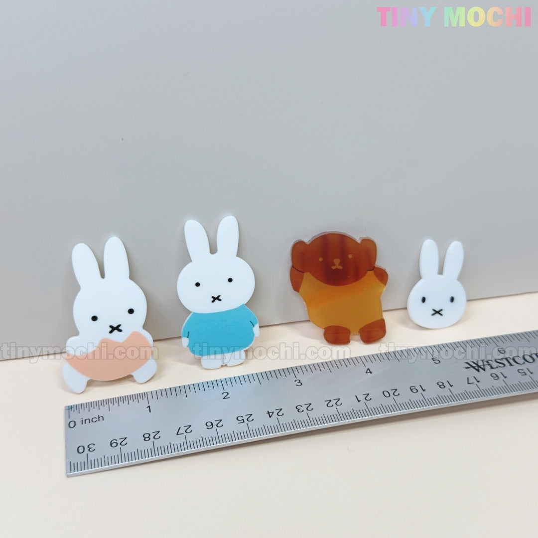 Four Kawaii Bunny & Bear Acrylic Hair Clips by Tiny Mochi—an orange bunny, blue bunny, brown bear, and small bunny face—are lined up by a ruler. The “Tiny Mochi” logo appears at the top right.