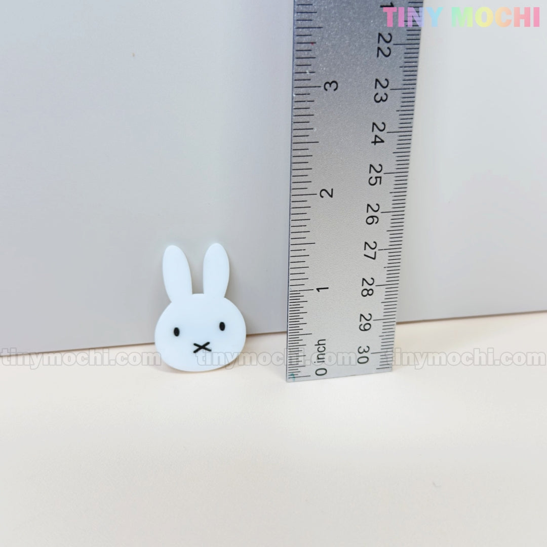 A small white bunny face charm from Tiny Mochis Kawaii Bunny & Bear Acrylic Hair Clips, perfect for cute animal hair accessories, is shown near a ruler at about 2.5 cm tall with Tiny Mochi in pastel on a light background.