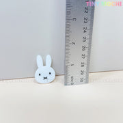 A small white bunny face charm from Tiny Mochis Kawaii Bunny & Bear Acrylic Hair Clips, perfect for cute animal hair accessories, is shown near a ruler at about 2.5 cm tall with Tiny Mochi in pastel on a light background.