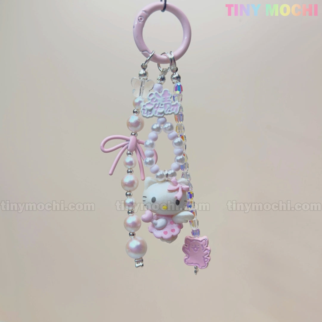 The Kawaii Pink Pearl Keychain by Tiny Mochi features a sweet kitty angel charm, pink pearl-like beads, a purple hedgehog accent, and a pink bow on a pink ring—perfect as a coquette phone or bag accessory. TINY MOCHI text appears in rainbow colors.