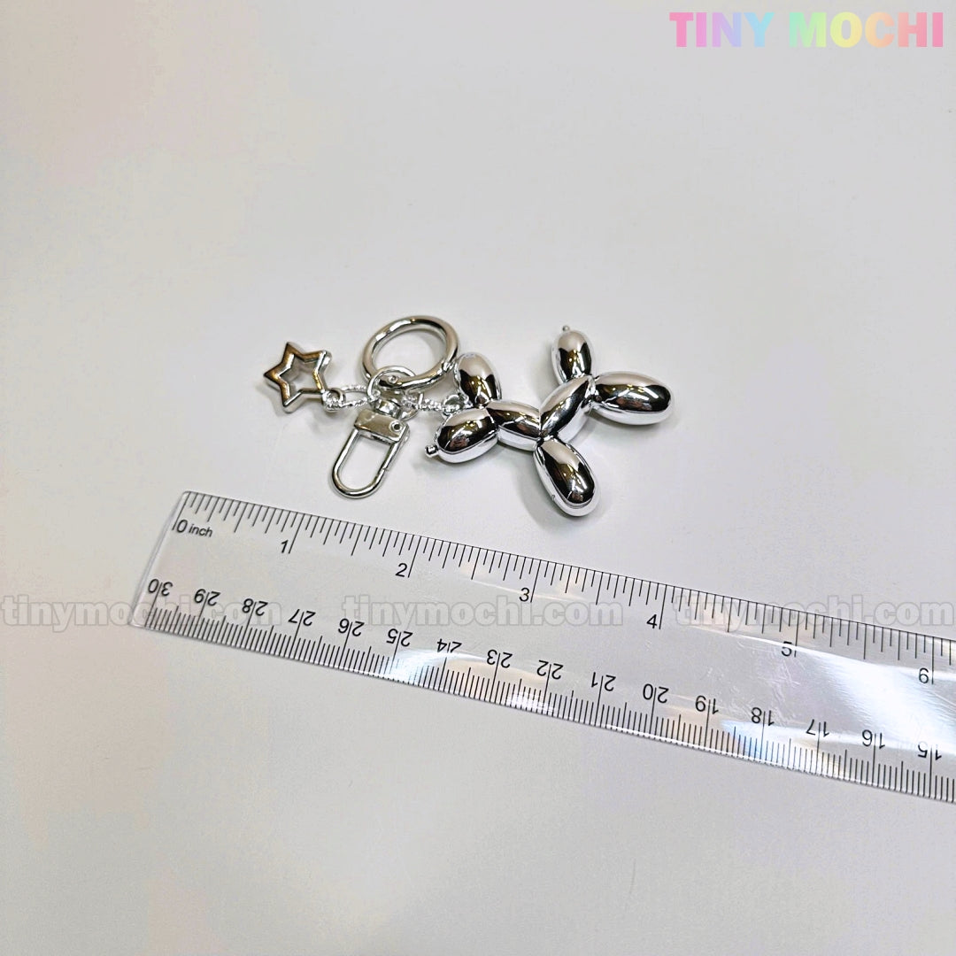 The Balloon Dog Keychain Silver Chrome Bag Charm with Star Accent by Tiny Mochi shines beside a clear ruler on a white surface, with the pastel Tiny Mochi logo in the top right, making it a cute metallic purse accessory gift.