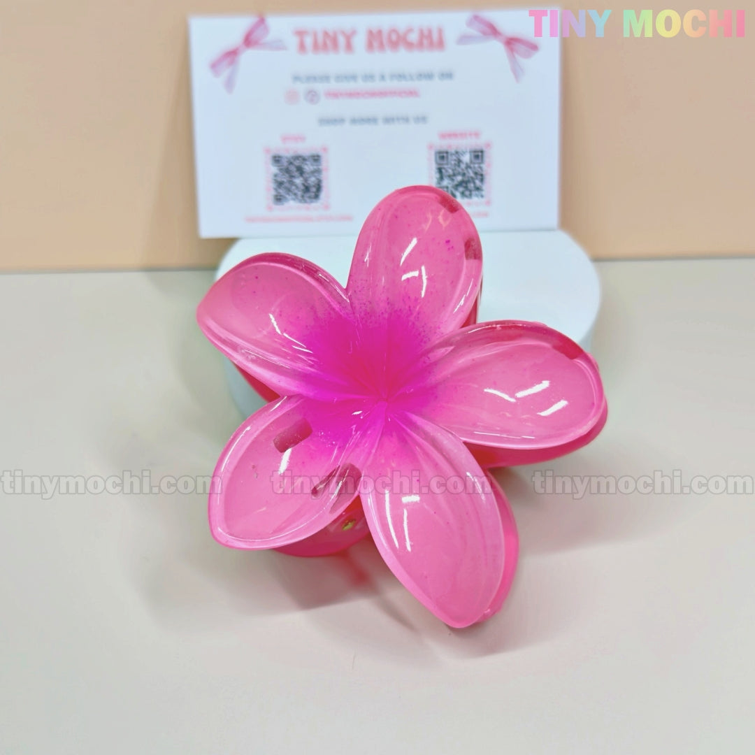 The Plumeria Flower Hair Claw by Tiny Mochi—a colorful floral hair clip for women and girls—rests on a white surface with a Tiny Mochi business card, making a stylish summer accessory for flower hair clip lovers.