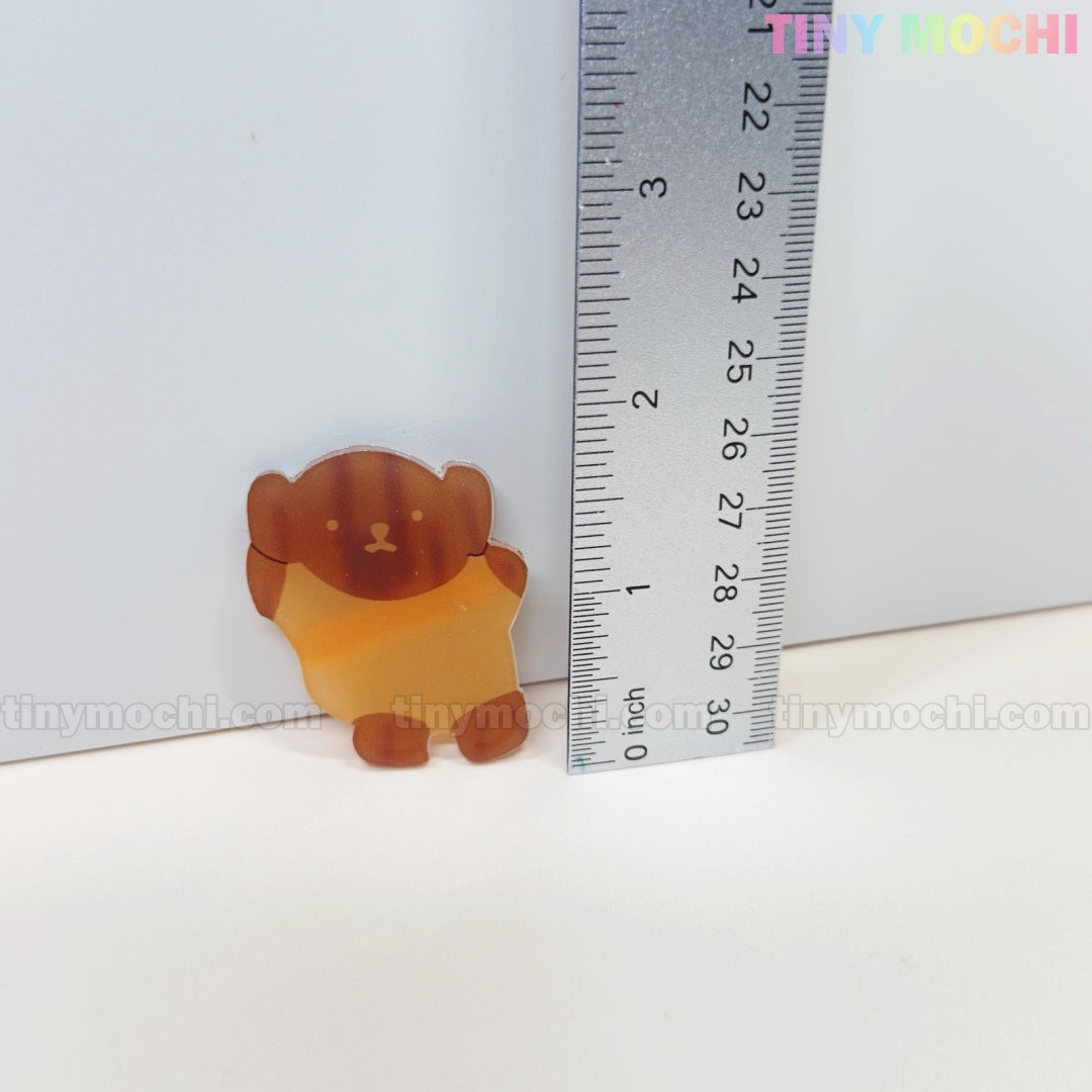 A small, brown bear-shaped acrylic hair clip from Tiny Mochi stands upright by a 4 cm ruler on a white background. TINY MOCHI in pastel colors highlights this cute accessory—ideal for fans of kawaii bunny and bear hair clips.