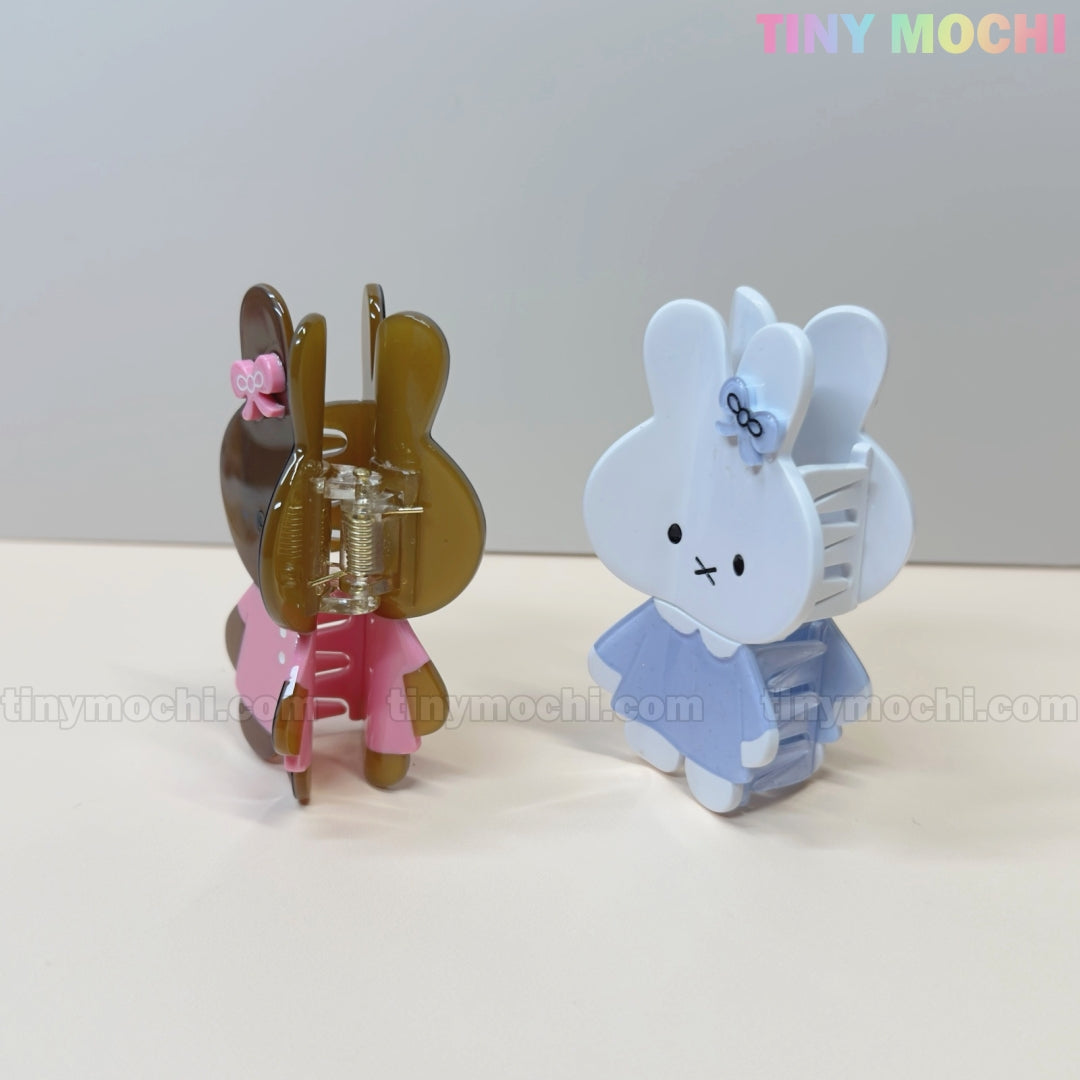 Two Kawaii Bunny Hair Claw Clips by Tiny Mochi stand on a light surface—one brown in pink, one white in blue. Each pastel acrylic clip features a cute bunny in a dress with a bow and cartoon face. TINY MOCHI is shown in the corner.