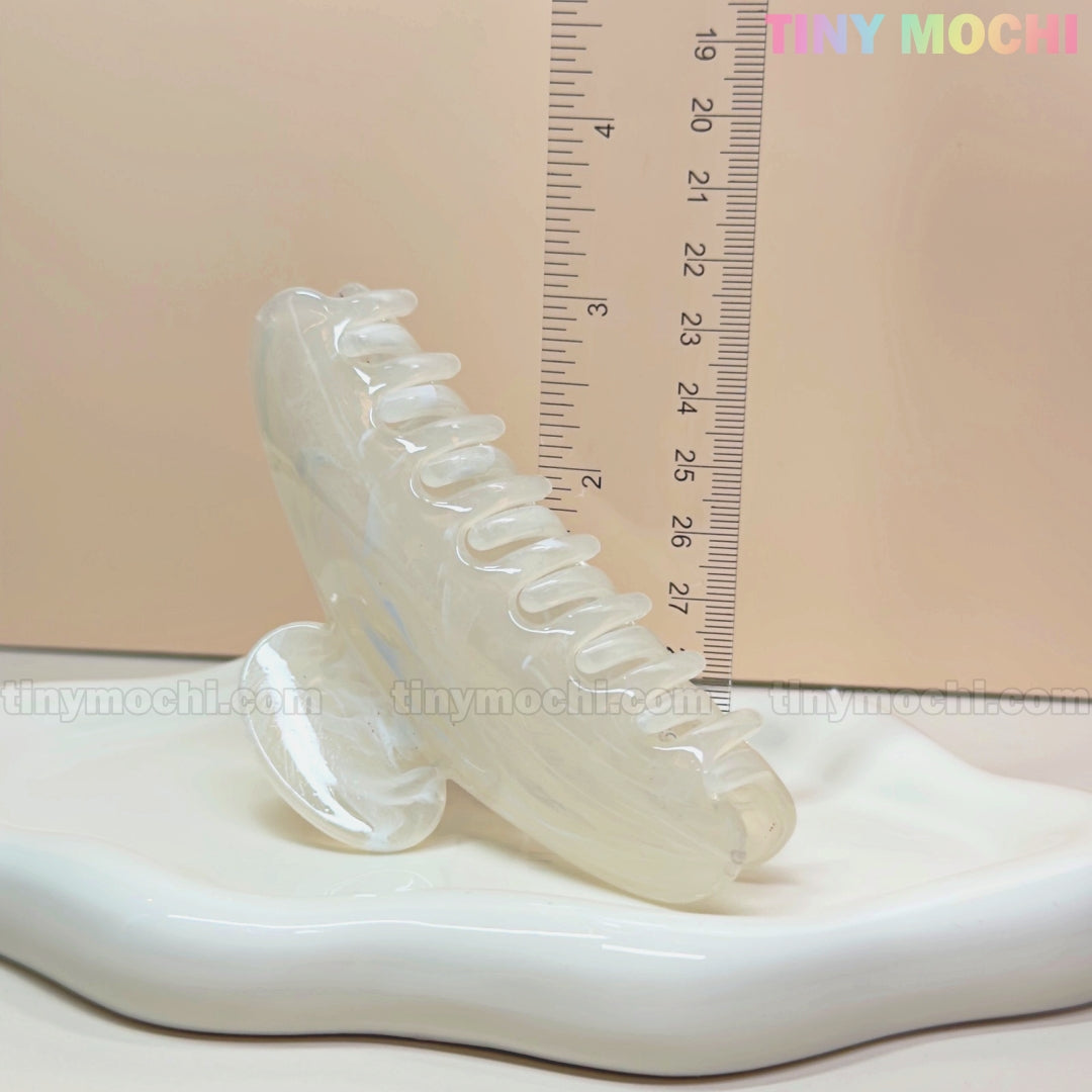The Large Marble Hair Claw Clip (11cm) by Tiny Mochi, a crescent-shaped pastel acrylic clip for thick hair, stands on a wavy dish with a clear ruler behind it; Tiny Mochi appears in pastel at the top right on a beige background.