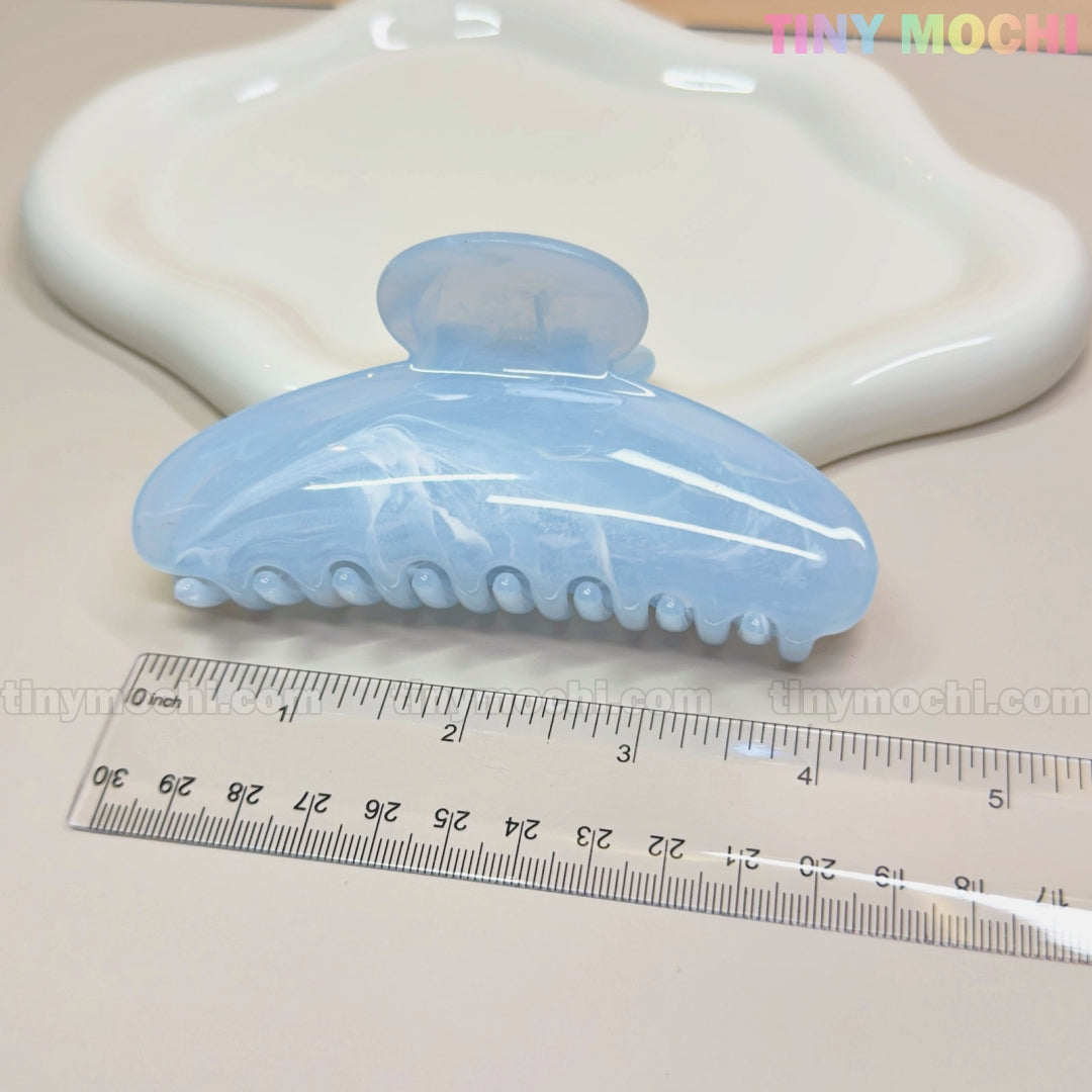 The Large Marble Hair Claw Clip 11cm by Tiny Mochi in pastel blue is shown next to a transparent ruler and a white wavy dish on a beige surface. The brand name, Tiny Mochi, appears in the top right corner.