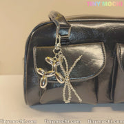 A shiny black handbag with two front pockets is styled with Tiny Mochi’s Silver Balloon Dog Keychain with Bead Bow, adding a trendy touch. The words TINYMochi and tinymochi.com are visible in the image.