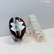 Two Kawaii Bunny Hair Claw Clips by Tiny Mochi rest on a light surface: one resembles a donut with sprinkles, the other is shaped like a croissant. Cute Hair Accessories by Tiny Mochi appears in colorful text at the top right against a plain background.