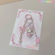 The Tiny Mochi Kawaii Pink Pearl Keychain features sweet kitty angel and bow charms with heart accents, perfect for a pastel coquette aesthetic. Displayed on a lace-patterned pastel pink card, its an adorable bag or phone accessory gift.