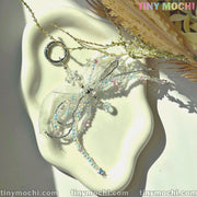 The Iridescent Beaded Bow Charm keychain by Tiny Mochi, featuring fairycore and coquette aesthetics, rests on a wavy white ceramic dish with dried flowers, capturing a bright, sunlit vibe perfect for whimsical style.