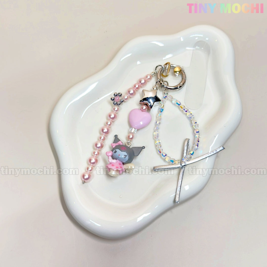 A white wavy dish holds three Kawaii Angel Charm Keychain Kits by Tiny Mochi, featuring pearls, ribbons, stars, a small Kuromi charm, clear beads with a silver cross, and pink accents. TINY MOCHI appears in the top right corner.