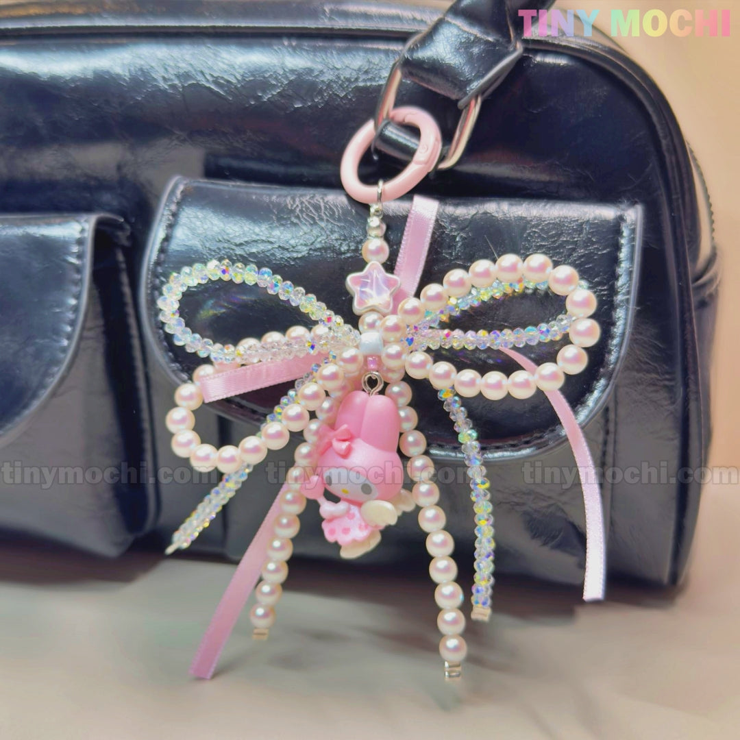 A shiny black bag features Tiny Mochis Kawaii Bow Charm Keychain, adorned with pearls, ribbon, and small cute charms like a pink bear and star—a perfect coquette angel accessory or DIY phone gift. TINY MOCHI is in the top right corner.