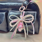 A shiny black bag features Tiny Mochis Kawaii Bow Charm Keychain, adorned with pearls, ribbon, and small cute charms like a pink bear and star—a perfect coquette angel accessory or DIY phone gift. TINY MOCHI is in the top right corner.