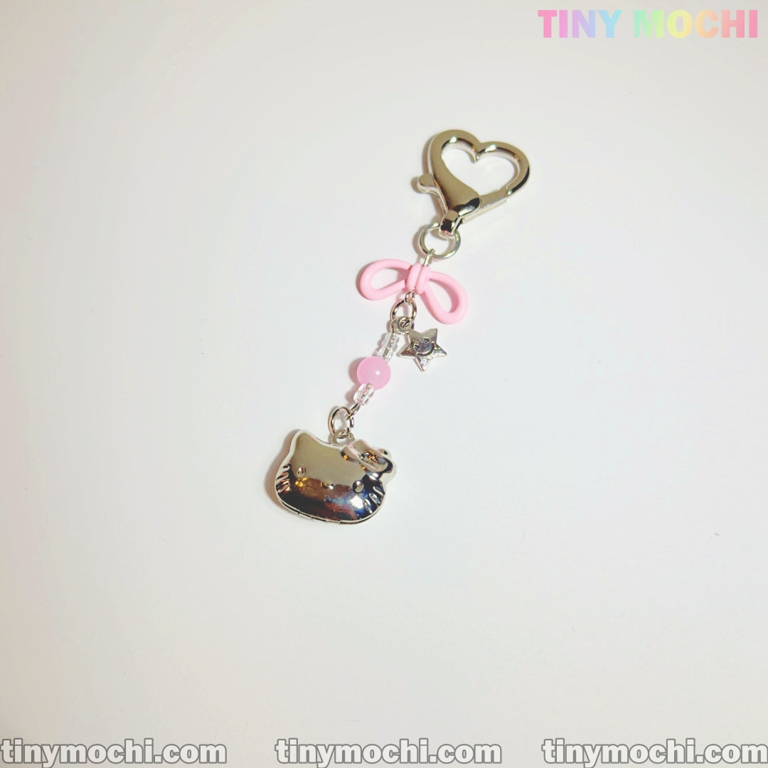 The Pink Kitty Bow Charm by Tiny Mochi is a cute phone or bag accessory featuring a silver heart clasp, pink bow and bead, silver star, and shiny kitty charm—perfect for coquette lovers. Displayed on white with Tiny Mochi branding.