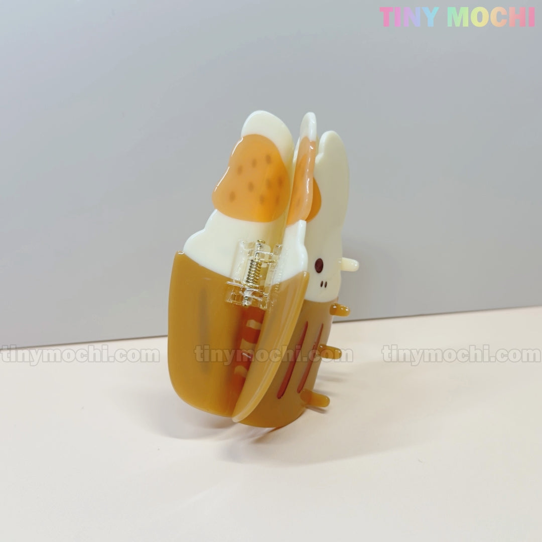 The Tiny Mochi Kawaii Cupcake Bunny Hair Claw Clip features a brown and white cartoon bunny with orange accents, displayed on a pale background with TINY MOCHI in pastel text at the top right corner.