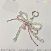 The Iridescent Crystal Bow Charm by Tiny Mochi features clear and pink crystals with a pink bear center, embodying Y2K style. Shown on a white background with the Tiny Mochi logo in the top right corner. Perfect for bags and phones.