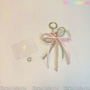 The Pearl Bow Bag Charm Beaded Keychain by Tiny Mochi, featuring pink ribbon, pearls, and a metal ring, adds a cute vintage touch to purses or backpacks. tinymochi.com and TINY MOCHI are displayed in pastel at the corners.