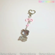 The Pink Kitty Bow Charm by Tiny Mochi is a cute phone and bag accessory for coquette lovers, featuring a silver cat-shaped locket, pink bow, heart-shaped clasp, and dangling charms. Pastel Tiny Mochi branding appears at the top right.