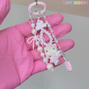 A hand in pink gloves holds the Kawaii Pink Pearl Keychain by Tiny Mochi, featuring a sweet white kitty angel charm, pink bow, pearl and crystal beads, with a pastel neutral background and the brand’s playful label.