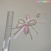 The Tiny Mochi Kawaii Bow Charm Keychain with pearl and ribbon makes a cute Coquette Angel bag charm or DIY phone accessory gift. Shown beside a clear ruler and badge clip, with TINY MOCHI in pastel on a light surface.
