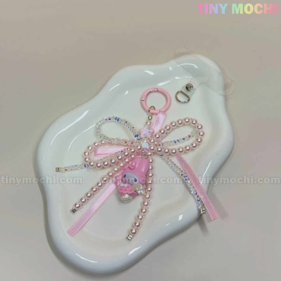 The Tiny Mochi Kawaii Bow Charm Keychain features pink and pearl beads, a pink ribbon bow, and a small pink bear charm—perfect as a coquette angel bag charm or DIY phone accessory gift. Displayed on a white dish.