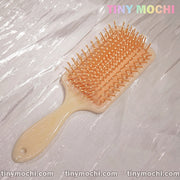 A Marble Pattern Detangling Brush by Tiny Mochi, styled in Nordic fashion for dry and wet hair, with beige bristles, rests on a shiny textured surface. Tiny Mochi appears in pastel colors at the top right corner.