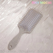 A Marble Pattern Detangling Brush - Nordic Style Paddle Hair Brush for Dry and Wet Hair by Tiny Mochi sits on a light, textured surface. TINY MOCHI appears in pastels at the top right; tinymochi.com repeats along the bottom edge.