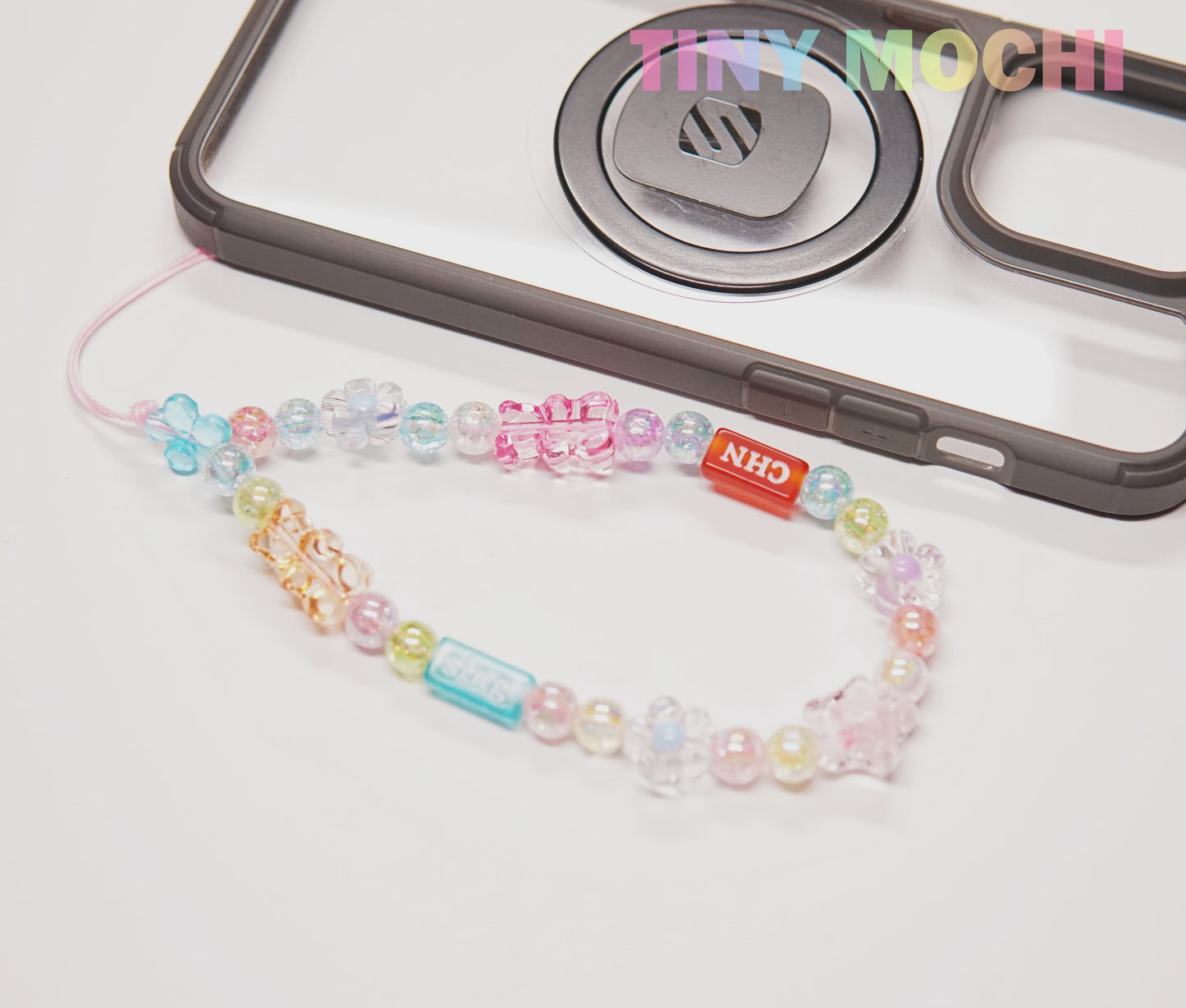 The Y2K Aesthetic Phone Charms Set by Tiny Mochi, featuring bear, butterfly, and heart charms on colorful lanyards, pops against the pastel Tiny Mochi logo atop a black and clear case for an on-trend retro vibe.