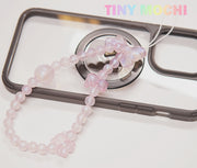 The Tiny Mochi Y2K Inspired Beaded Phone Strap Collection features pink butterfly and round beads, adding a trendy touch to black or clear phone cases. TINY MOCHI appears in pastel rainbow letters in the top right corner.