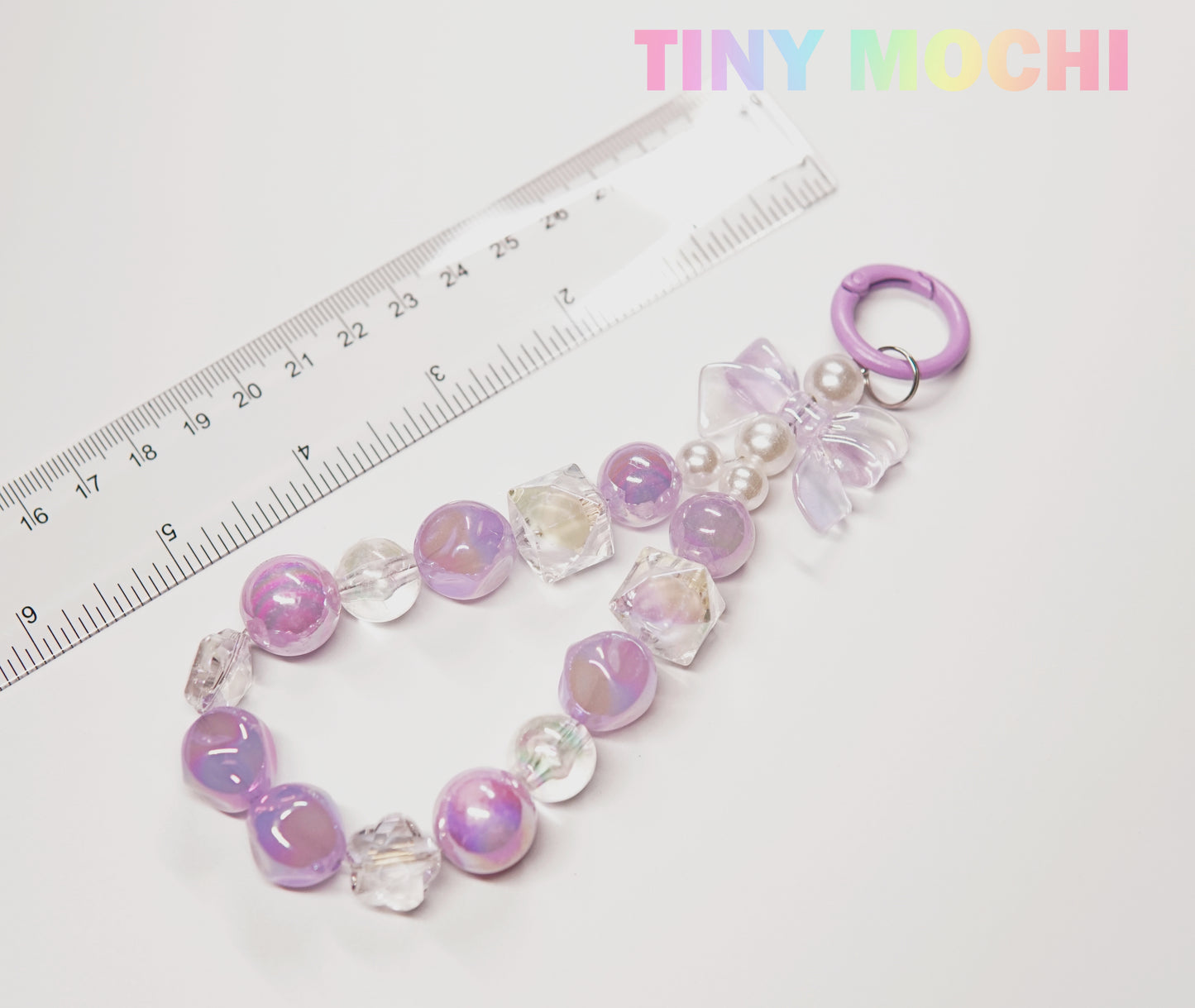 The Tiny Mochi Adorable Faux Pearl Bag Charm Keyring is shown next to a ruler and under pastel branding, featuring faux pearls, a bow, and a round clasp—perfect as a cute backpack companion.