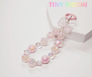 The Adorable Faux Pearl Bag Charm Keyring by Tiny Mochi features faux pearls, a pink clasp, and a cute bow on a white surface. Perfect as a backpack companion or phone charm. TINY MOCHI is displayed in rainbow colors in the top right corner.