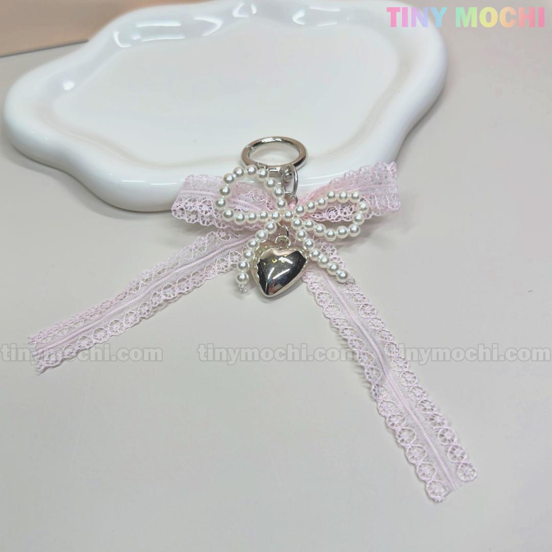 A cute Kawaii Lace Bow Keychain with pearl beads and a silver heart charm from Tiny Mochi, perfect as a bag charm, phone strap, or car mirror accessory. TINY MOCHI appears in pastel colors at the top right on a white decorative plate.