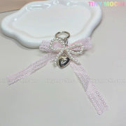 A cute Kawaii Lace Bow Keychain with pearl beads and a silver heart charm from Tiny Mochi, perfect as a bag charm, phone strap, or car mirror accessory. TINY MOCHI appears in pastel colors at the top right on a white decorative plate.