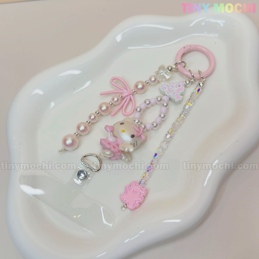 The Kawaii Pink Pearl Keychain by Tiny Mochi, featuring a Sweet Kitty Angel charm, pink bow, and cute beads, is displayed on a wavy white tray. Ideal for coquette and kawaii style fans; the photo includes a Tiny Mochi watermark.