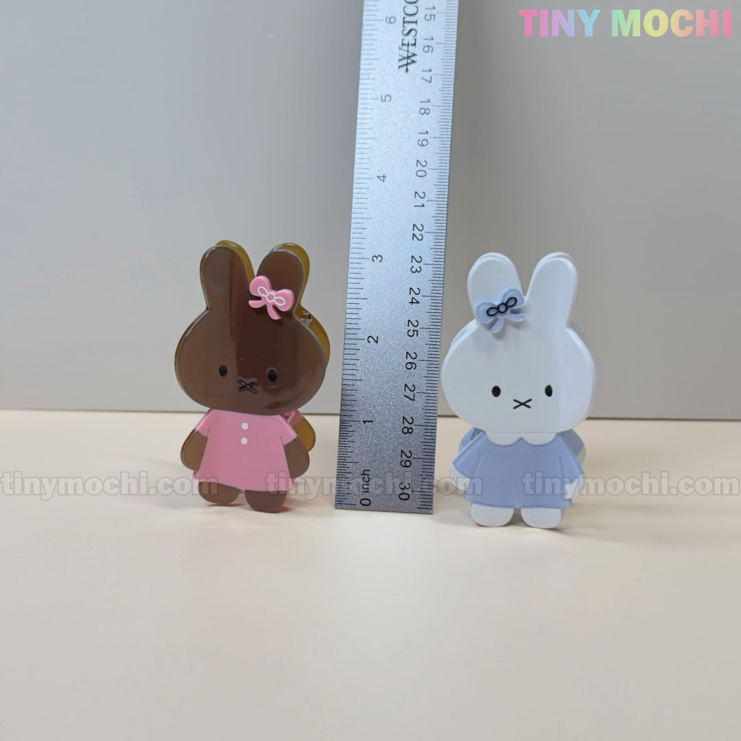 Two adorable bunny hair claw clips by Tiny Mochi, one brown in a pink dress and one white in a blue dress with bows, stand at about 8 cm tall—perfect pastel acrylic accessories for any kawaii fan!.