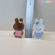 Two adorable bunny hair claw clips by Tiny Mochi, one brown in a pink dress and one white in a blue dress with bows, stand at about 8 cm tall—perfect pastel acrylic accessories for any kawaii fan!.