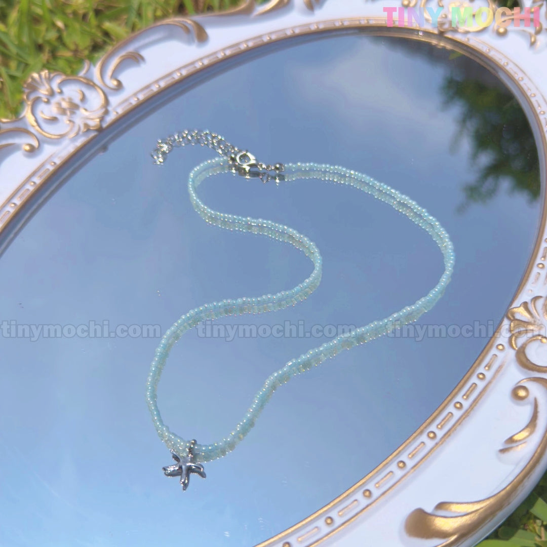 The Silver Starfish Choker Necklace by Tiny Mochi features light blue beads and a dainty starfish charm—perfect oceancore beach jewelry and a handmade gift for girls or teens.