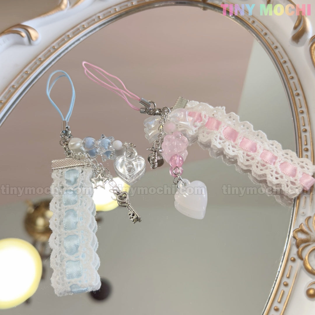 Two Kawaii Pastel Lace Ribbon Keychains by Tiny Mochi, one blue and one pink, with beads, heart & star charms, lay on a mirror. Perfect fairycore accessories. The pastel Tiny Mochi logo appears at the top right.