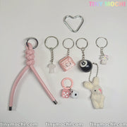 The Tiny Mochi Cute Bunny and Charm Keychain features eight kawaii accessories, including a pink braided strap, heart-shaped ring, Y2K lock, 8-ball, dice, plush bunny, and two cute character charms—perfect for purses and backpacks.