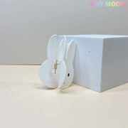 The Kawaii Bunny Face Hair Clip – White Rabbit Claw Clip by Tiny Mochi stands upright beside a white block on a neutral background, with TINY MOCHI in colorful letters at the top right and its metal spring visible.