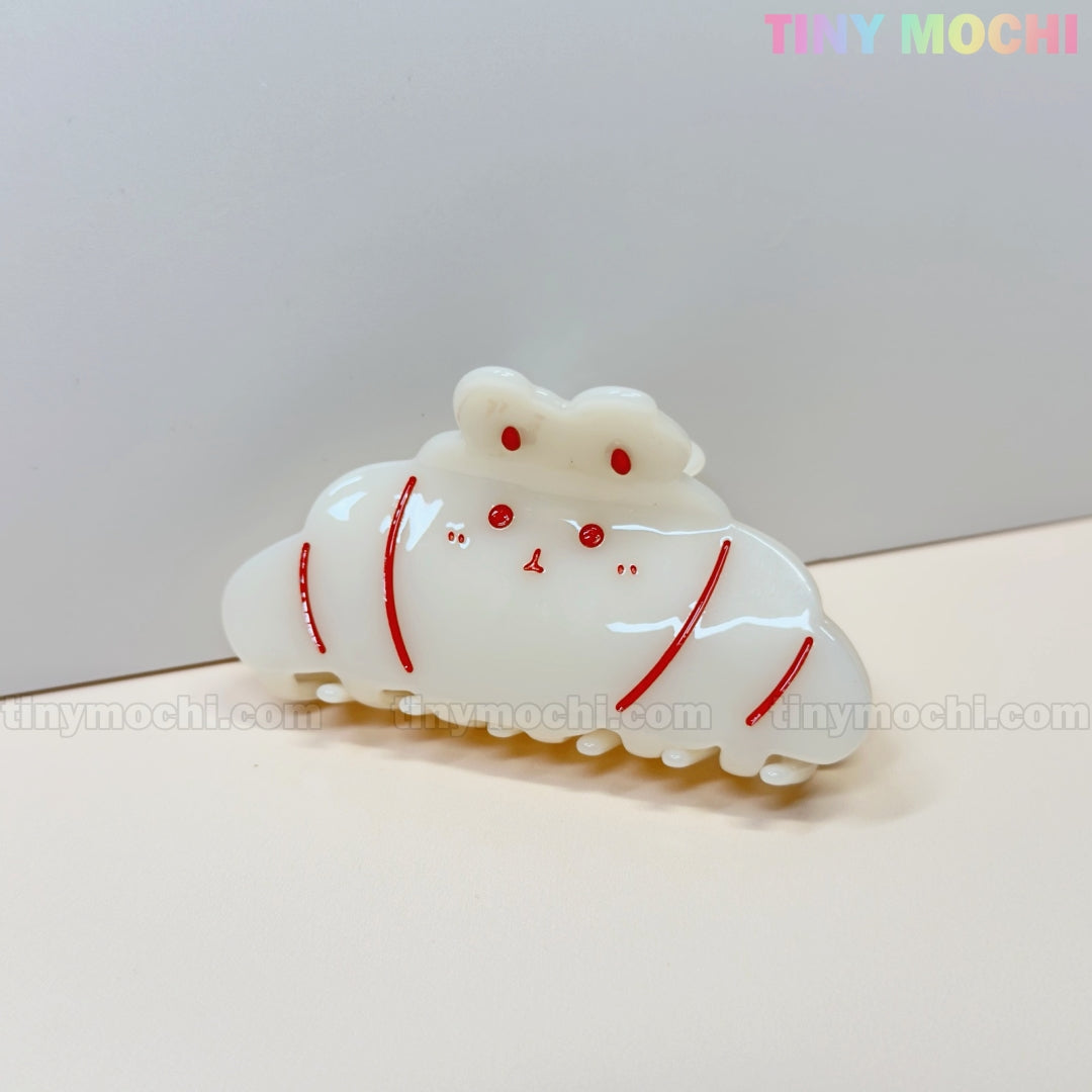The Kawaii Bunny Hair Claw Clip by Tiny Mochi features a croissant-shaped acrylic design with a cute face and red lines, making it an adorable addition to your collection of cute hair accessories.