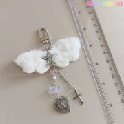 The Fluffy Angel Wing Keychain – Star & Cross Bag Charm Clip by Tiny Mochi features white wings and silver charms, channeling a soft gothic angel vibe. Shown near a clear ruler on a light surface, with “Tiny Mochi” in pastel at the top right.