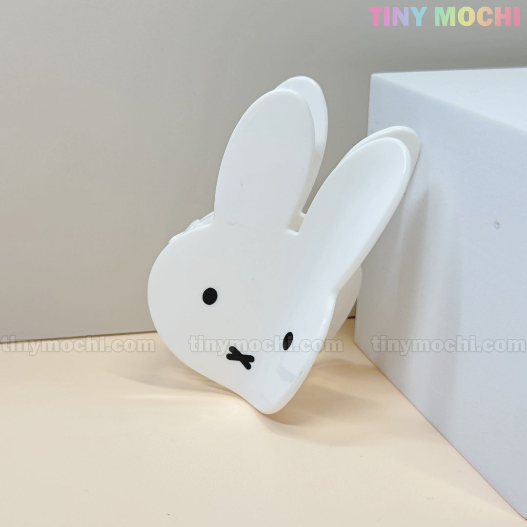 The Kawaii Bunny Face Hair Clip – White Rabbit Claw Clip by Tiny Mochi features a white bunny face with black eyes and an X mouth, leaning against a white block—a perfect kawaii accessory for any look.