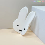 The Kawaii Bunny Face Hair Clip – White Rabbit Claw Clip by Tiny Mochi features a white bunny face with black eyes and an X mouth, leaning against a white block—a perfect kawaii accessory for any look.