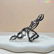The Tiny Mochi Dark Silver Crystal Heart Hair Claw, an elegant metal hair clip for women with clear and pink gemstones, is displayed on a white ceramic tray against a light beige background. TINY MOCHI appears in the top right corner.