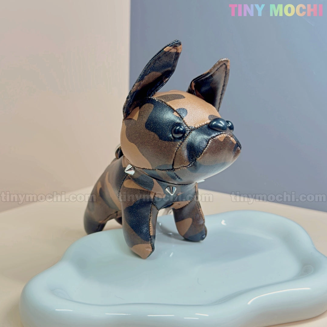 A mini French Bulldog keychain coin purse by Tiny Mochi, made of faux leather with a cute studded collar, stands on a glossy cloud-shaped surface—an adorable zipper pouch and bag charm gift for dog lovers. Pastel background features Tiny Mochi branding.