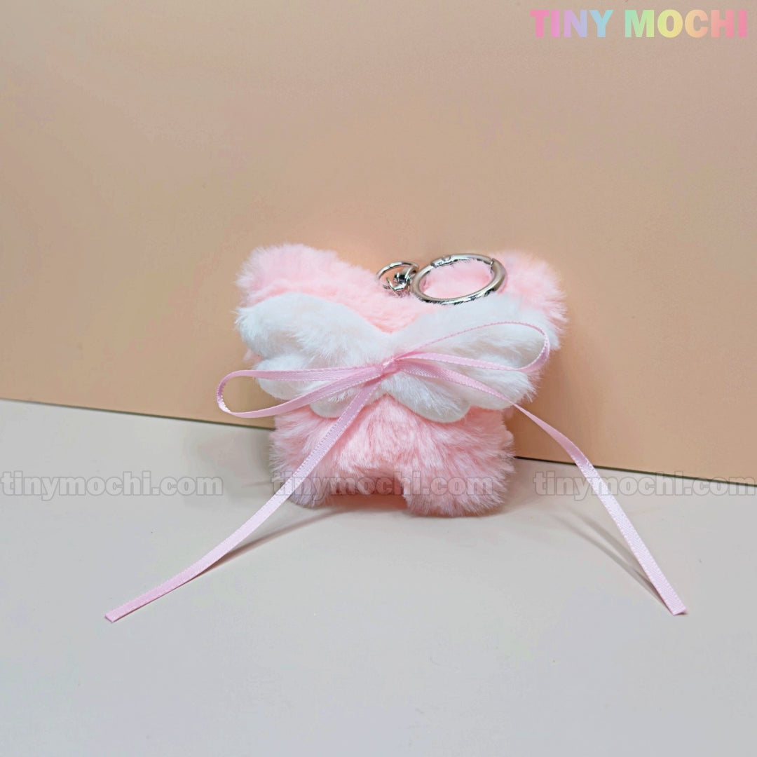 A soft, pink Plush Butterfly Bow Keychain from Tiny Mochi, with white wings and a light pink ribbon bow—perfect for coquette and kawaii lovers. Shown on a pastel background, TINY MOCHI is in the top right corner.